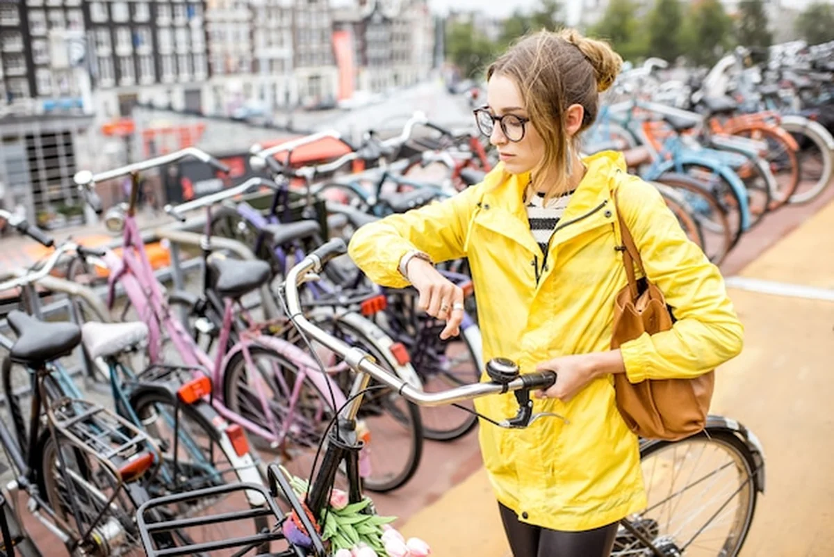 Młoda kobieta turystka w żółtym płaszczu parkująca rower w Amsterdamie