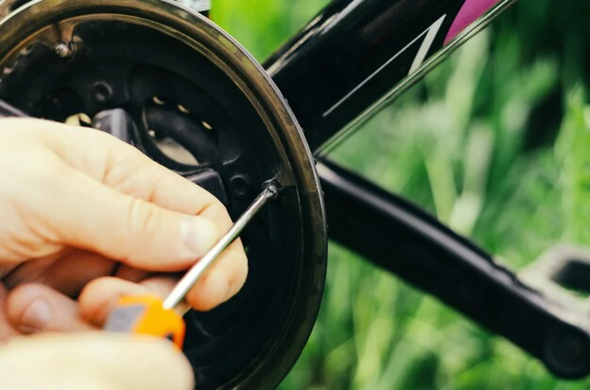 Mężczyzna odkręca śruby pomarańczowym śrubokrętem na łańcuchu roweru górskiego